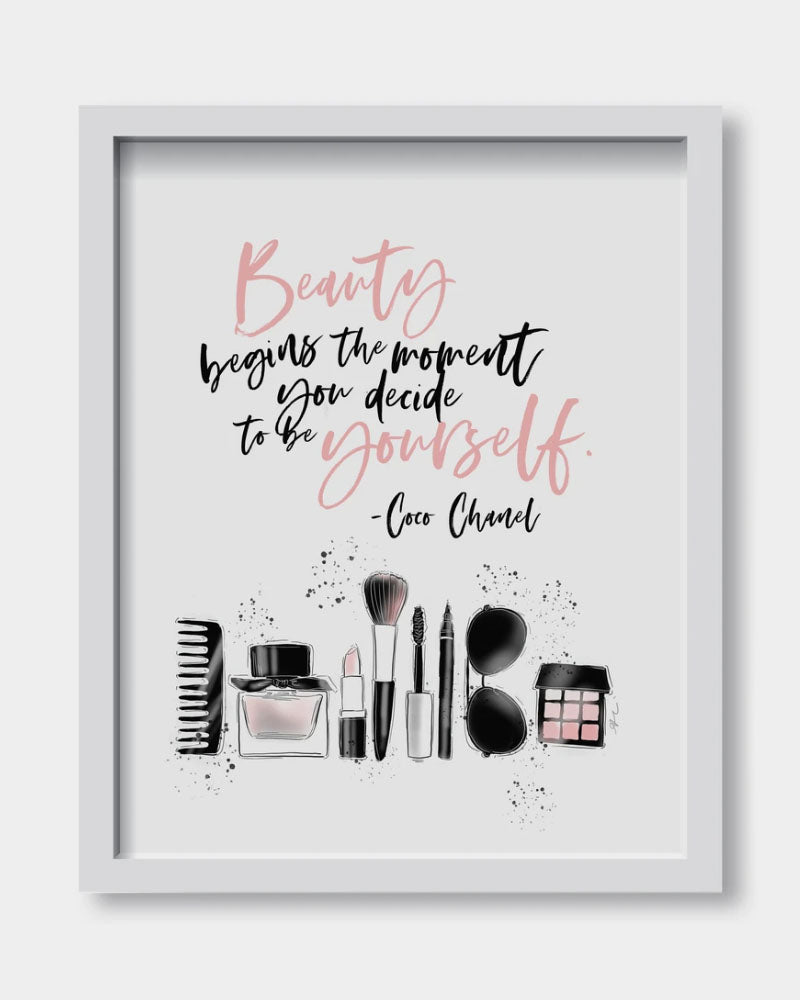 Art print with the words beauty begins the moment you decide to be yourself, written in black and pink cursive with makeup products on the bottom of the print on a white background