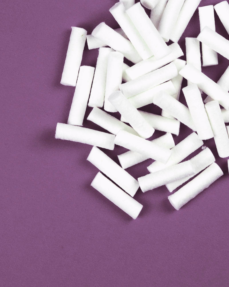white, short cotton rolls in a pile on a purple background